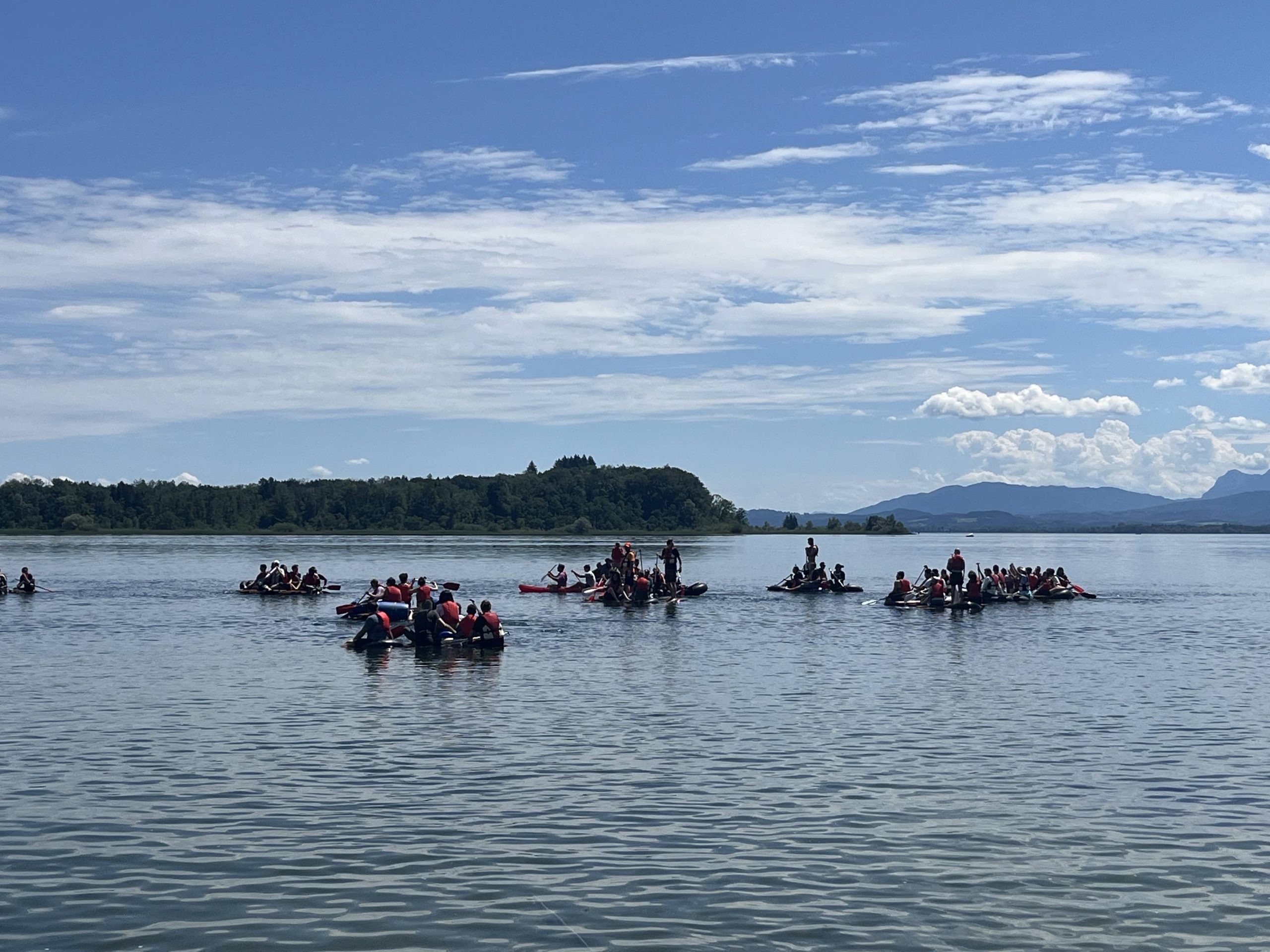 Mehrere selbstgebaute Flöße mit Teams in roten Schwimmwesten auf dem Bodensee beim Teamevent