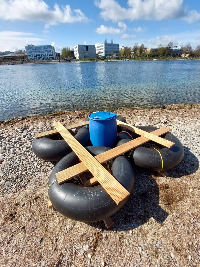 Selbstgebautes Floß aus Reifenschläuchen, Holzbalken und Fass am Ufer des Bodensees